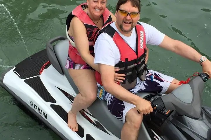 Two people smiling while sitting on a Yamaha jet ski in water.