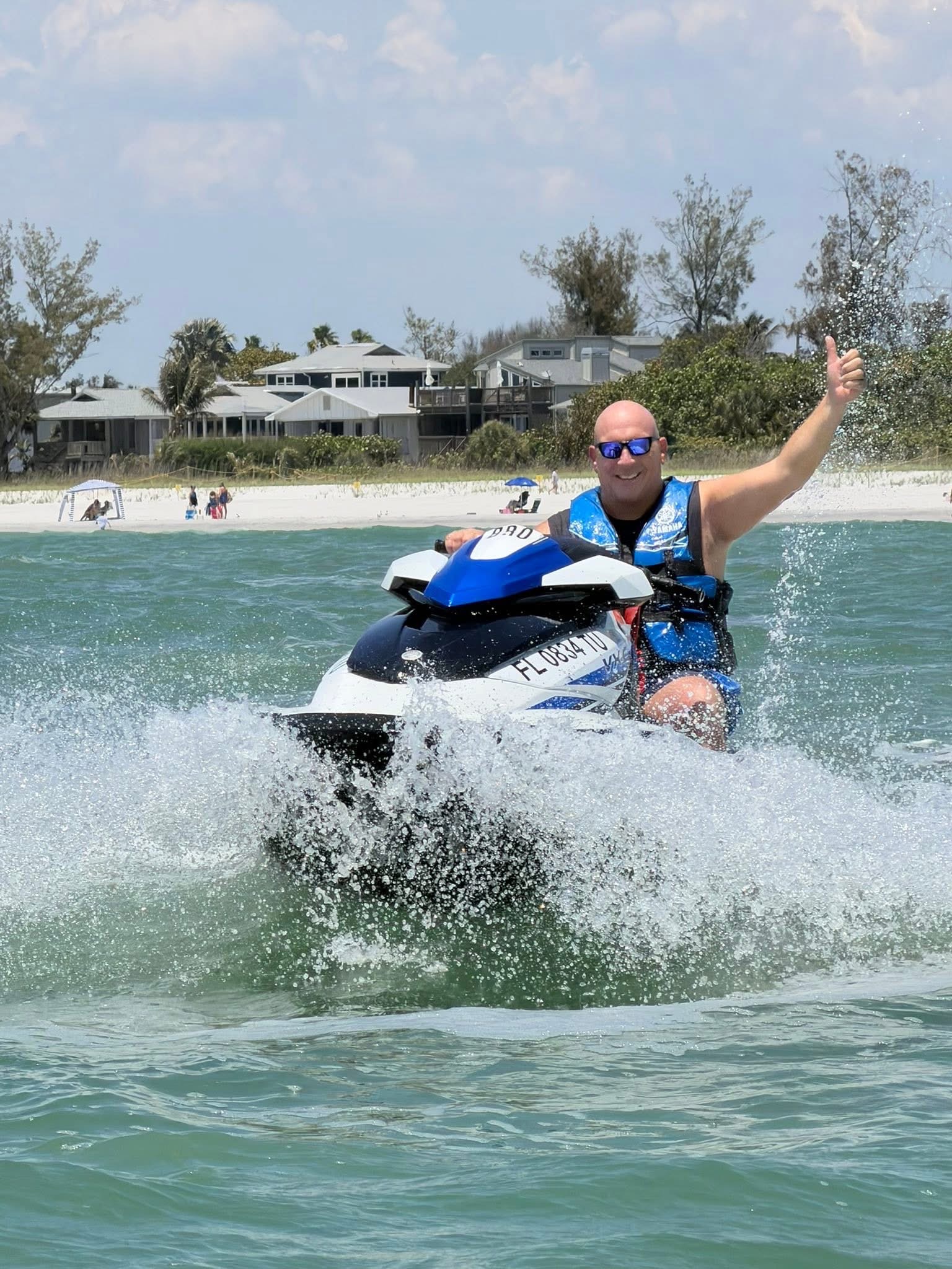 Person on a jet ski giving a thumbs-up near a beach.