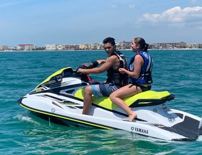 Two people riding a jet ski on the ocean near a coastal city.