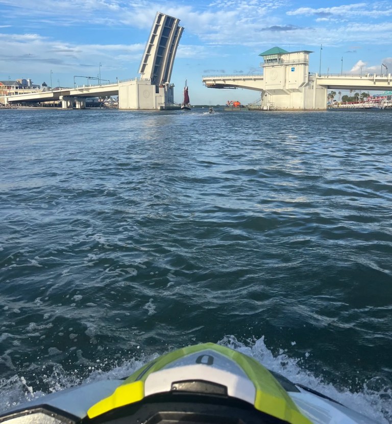 Open drawbridge over a river with a jet ski in the foreground.